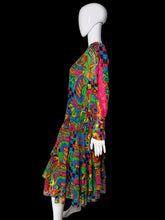 Load image into Gallery viewer, A long-sleeve tiered dress displayed on a white mannequin, featuring a highly vibrant, multicolored psychedelic abstract pattern with swirls, paisley, and checkerboard motifs.

