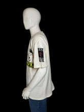 Load image into Gallery viewer, A white graphic t-shirt displayed on a white mannequin from the side. The shirt features a black and white graphic on the front with yellow text, and a black sleeve print reading 'BLACK LITE' with a pink symbol.
