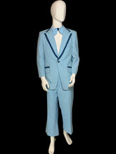 Load image into Gallery viewer, A light blue suit displayed on a white mannequin. The suit features dark blue contrast piping along the lapels and pocket edges, and is styled with a matching light blue bow tie and white dress shirt.
