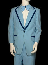 Load image into Gallery viewer, A light blue suit displayed on a white mannequin. The suit features dark blue contrast piping along the lapels and pocket edges, and is styled with a matching light blue bow tie and white dress shirt.
