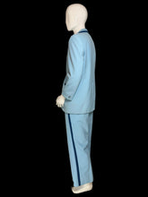 Load image into Gallery viewer, A light blue suit displayed on a white mannequin. The suit features dark blue contrast piping along the lapels and pocket edges.

