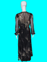 Load image into Gallery viewer, A black long-sleeve maxi dress with sheer mesh sleeves and a metallic gold abstract floral pattern, displayed on a white mannequin.
