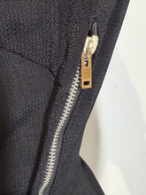 Load image into Gallery viewer, Close-up of a black textured fabric garment with a silver zipper and a small gold-toned metal pull tab.
