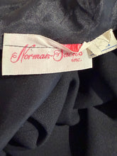 Load image into Gallery viewer, Close-up of a black fabric garment showing a cream paper label with red script reading 'Norman-Sacks inc.'

