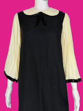 Load image into Gallery viewer, A black dress displayed on a white mannequin, featuring cream pleated three-quarter sleeves with black trim.
