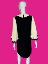 Load image into Gallery viewer, A back view of a black dress displayed on a white mannequin, featuring three-quarter pleated cream sleeves with black trim.

