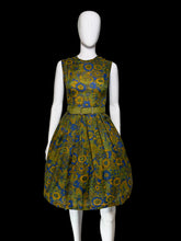 Load image into Gallery viewer, A sleeveless knee-length dress with a pleated skirt and matching belt, featuring a bold floral pattern in olive green, mustard yellow, and blue, displayed on a white mannequin.
