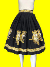 Load image into Gallery viewer, A black pleated skirt displayed on a white mannequin, featuring large printed leopard prints in yellow, white, and black, with matching leopard and floral patterned trim at the waistband and hem.
