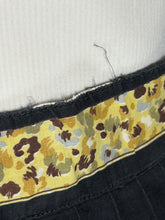 Load image into Gallery viewer, Close-up of a garment's waistband showing a yellow leopard print fabric band with brown, black, and gray spots, bordered by black fabric with some fraying.
