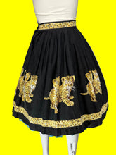 Load image into Gallery viewer, A black pleated skirt with gold leopard prints and decorative gold patterned bands at the waist and hem, displayed on a white mannequin.
