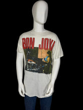 Load image into Gallery viewer, A vintage Bon Jovi graphic t-shirt displayed on a white mannequin. The t-shirt is off-white with a large red 'BON JOVI' logo and a graphic print of a motorcycle.
