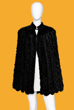 Load image into Gallery viewer, A black textured velvet cape with a high collar and button closure, displayed on a white mannequin against a plain off-white wall.
