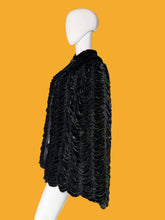 Load image into Gallery viewer, A black textured velvet cape jacket with a ruffled scalloped hem, displayed on a white mannequin.
