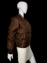 Load image into Gallery viewer, A brown quilted bomber jacket displayed on a white mannequin. The jacket features gold-colored piping details and ribbed knit collar, cuffs, and hem.
