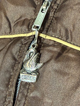 Load image into Gallery viewer, Close-up of a brown quilted jacket with a silver zipper and a swan-shaped zipper pull featuring the word 'COMFY' on a block.
