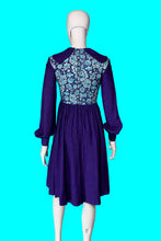 Load image into Gallery viewer, A long sleeve blue mini dress with a light blue and silver psychadelic print on the bodice and a dramatic collar shown from the back on a white mannequin.
