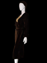 Load image into Gallery viewer, A dark brown velvet 1920s set featuring a midi length dress and matching long sleeve cropped jacket displayed on a white mannequin. The set includes a matching brown head covering. 
