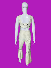 Load image into Gallery viewer, A cream-colored two-piece outfit displayed on a white mannequin. The set includes a sleeveless crop top with black dashed trim and matching high-waisted flared pants with black dashed trim and decorative buttons on the back.
