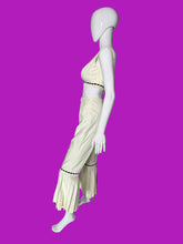 Load image into Gallery viewer, A cream-colored two-piece outfit displayed on a white mannequin. The set includes a sleeveless crop top with black dashed trim and matching high-waisted flared pants with black dashed trim and decorative buttons on the back.
