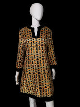 Load image into Gallery viewer, A women's tunic dress shown on a white mannequin. The dress features a bold geometric chain-link pattern in orange, black, and beige, with solid black trim at the split neckline, cuffs, and hem.
