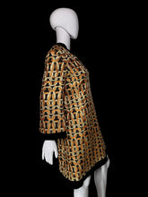 Load image into Gallery viewer, A women's tunic dress shown on a white mannequin. The dress features a bold geometric chain-link pattern in orange, black, and beige, with solid black trim at the split neckline, cuffs, and hem.
