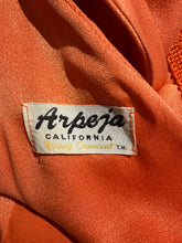 Load image into Gallery viewer, Close-up of an orange fabric garment with a sewn-on label reading 'Arpeja CALIFORNIA Young Innocent T.M.'
