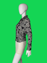 Load image into Gallery viewer, A long-sleeve button-up blouse with a black and white spiral swirl pattern, displayed on a white mannequin torso shown from the side. 
