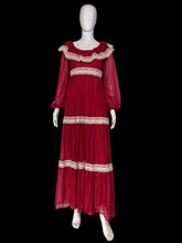 Load image into Gallery viewer, A long maroon chiffon and lace prairie dress displayed on a white mannequin from the front, featuring sheer long sleeves, a square neckline with cream lace trim, and matching lace bands at the waist and hem.
