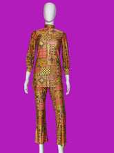 Load image into Gallery viewer, A two-piece matching set consisting of a long-sleeve mock-neck top and matching cropped pants, displayed on a white mannequin. The set features a vibrant, busy patchwork-style geometric print with orange, yellow, red, and black colors.
