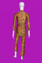 Load image into Gallery viewer, A two-piece matching long-sleeve top and pants set displayed on a white mannequin from the back. The fabric features a busy, colorful patchwork-style African wax print with geometric patterns in orange, yellow, red, and black.
