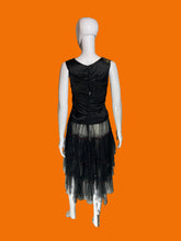 Load image into Gallery viewer, A sleeveless 1920s drop waist black dress with a sheer ruffled layered skirt shown on a white mannequin from the back. 
