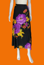 Load image into Gallery viewer, A black midi skirt with a vibrant purple, yellow, and orange floral print, displayed on a white mannequin against a solid black background.
