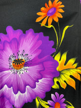 Load image into Gallery viewer, A close-up of a black fabric featuring a vibrant floral print with a large purple flower in the foreground, an orange flower on the left, and yellow leaves in the background.
