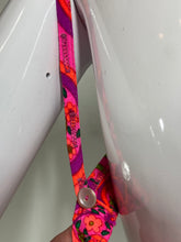 Load image into Gallery viewer, A close-up of a colorful floral-patterned strap, secured with a button against a glossy white background.
