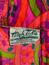 Load image into Gallery viewer, Close-up of a colorful patterned fabric with a sewn-on fabric label reading 'High Tide Swimwear From California'.
