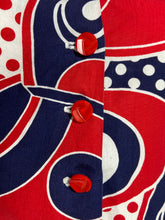 Load image into Gallery viewer, Close-up of a red, navy blue, and white patterned garment with three red buttons down the front.

