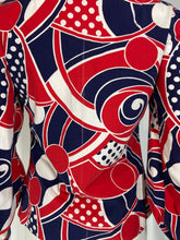 Load image into Gallery viewer, A close-up of a long-sleeve top featuring a bold abstract pattern in red, navy blue, and white, with swirls, polka dots, and curved geometric shapes.
